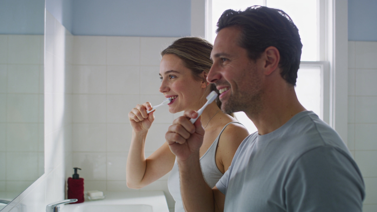 Man and woman brushing teeth together at a bathroom basin in the morning